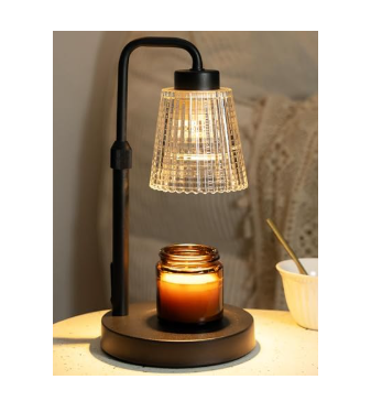Black metal electric candle warmer lamp featuring a clear fluted glass shade, illuminating and melting an amber jar candle on a speckled side table.