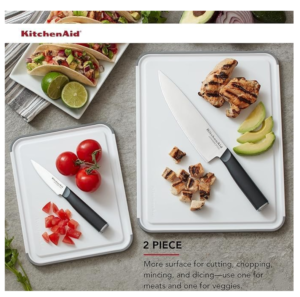 KitchenAid 2-piece cutting board set with grey non-slip edges, displaying tomatoes on one board and grilled chicken on the other to demonstrate separate use for produce and proteins.