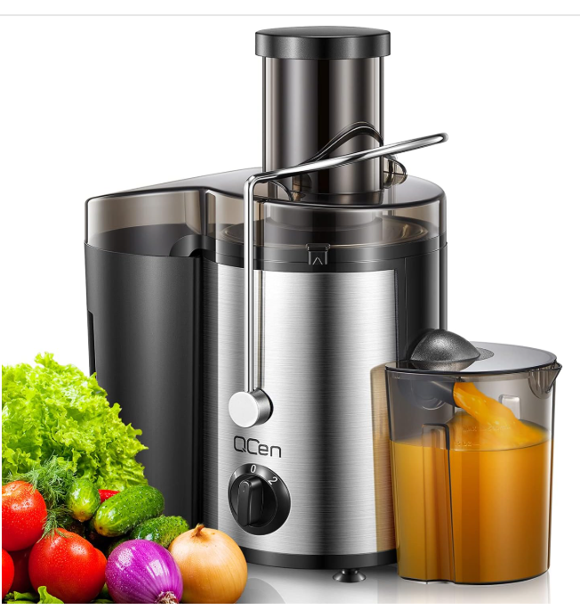 Stainless steel QCen centrifugal juicer with a 3-inch wide mouth feed chute, a two-speed control knob, a locking arm, and a juice pitcher filled with orange juice next to fresh vegetables.