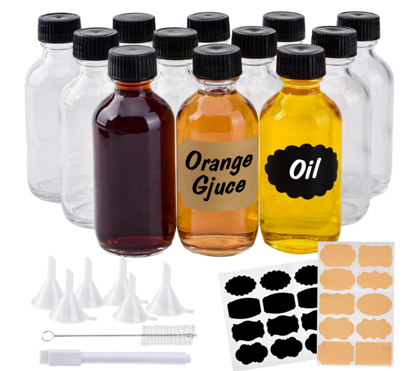 A set of small clear glass bottles with black caps, some filled with liquid, displayed with mini funnels, a cleaning brush, and sticker labels
