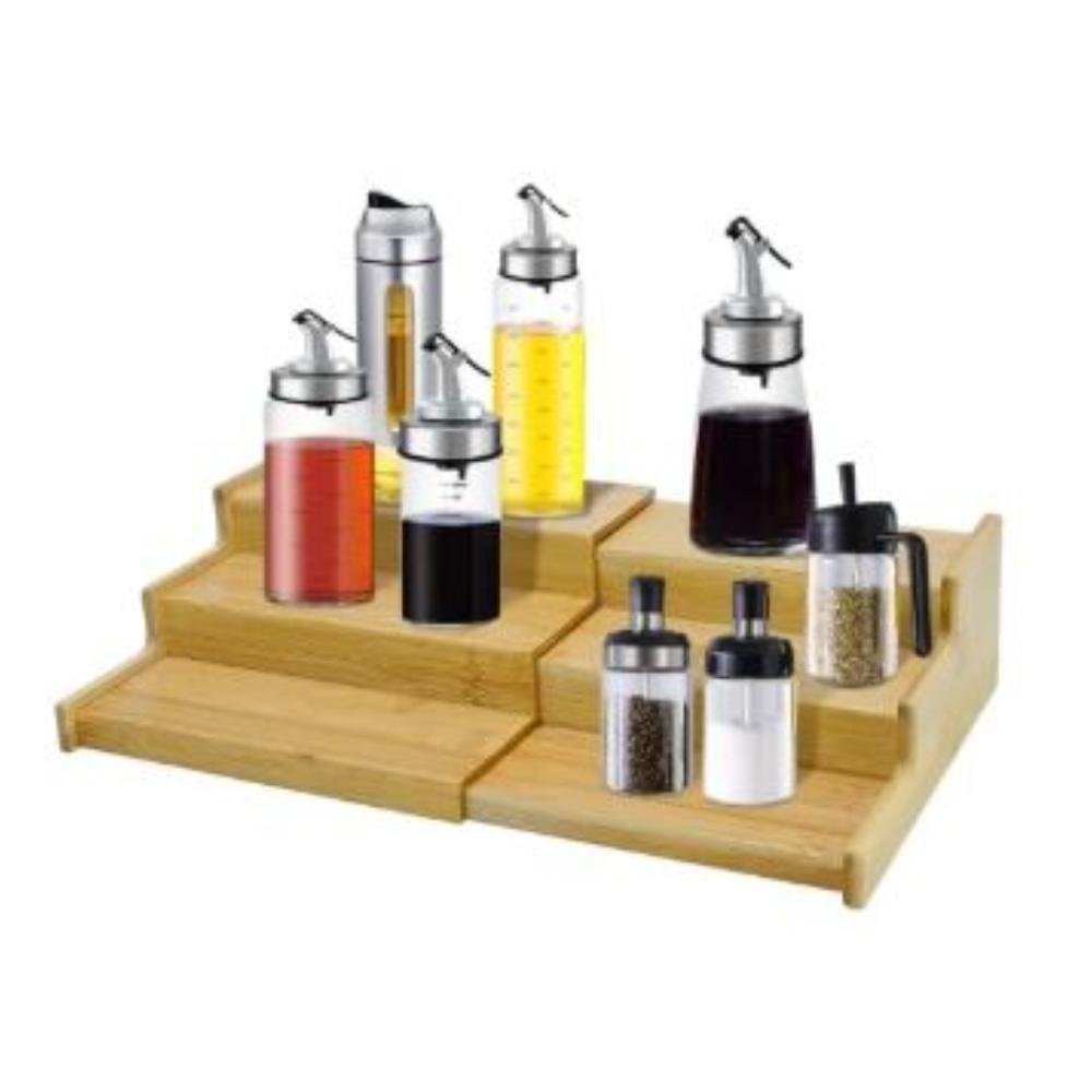 Bamboo 3-tier expandable spice rack holding glass bottles with metal pour spouts on kitchen counter