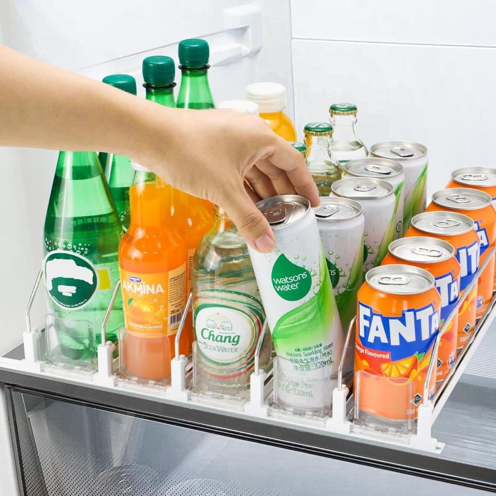 Hand reaching for beverage in clear plastic fridge organizer bin holding soda cans and bottles